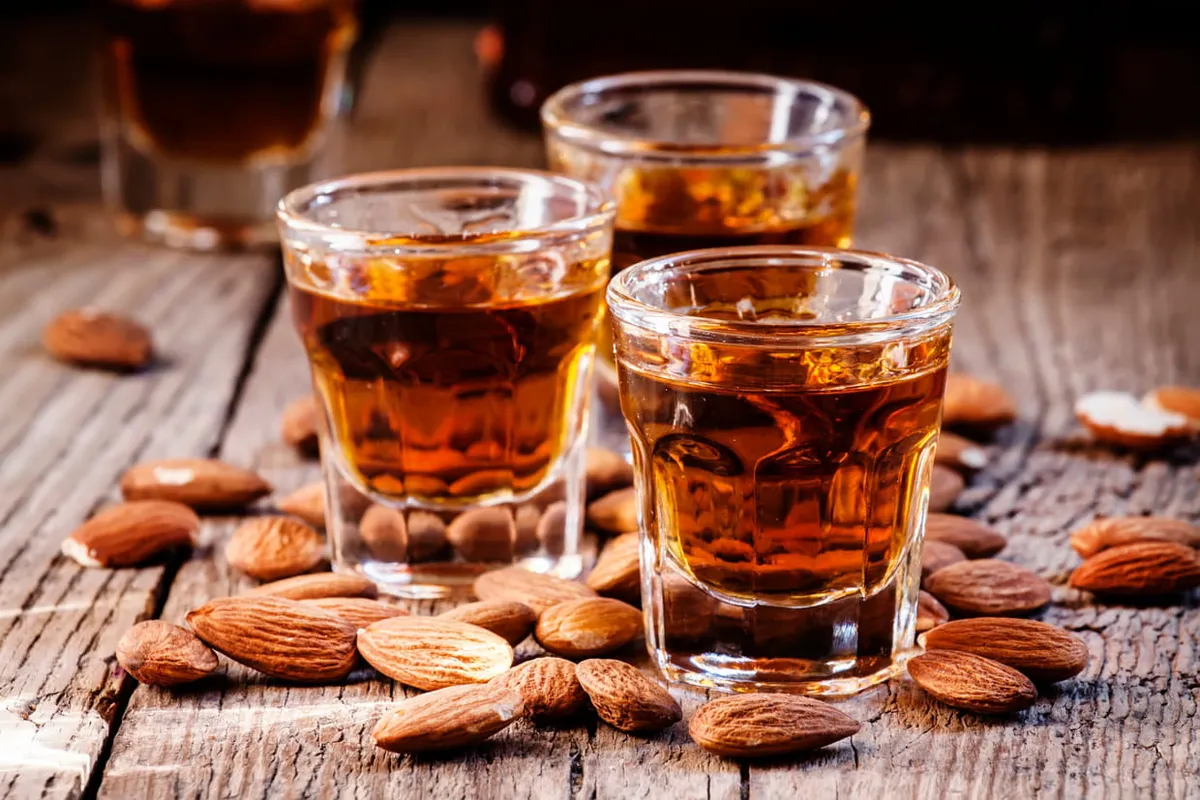 Bouteille d'amaretto maison posée sur une table en bois, verre à moitié rempli et quelques amandes éparpillées