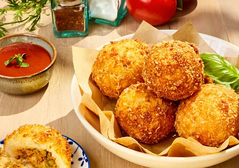 Des arancini dorés posés sur une assiette en céramique, avec un filet de sauce tomate et quelques feuilles de basilic frais
