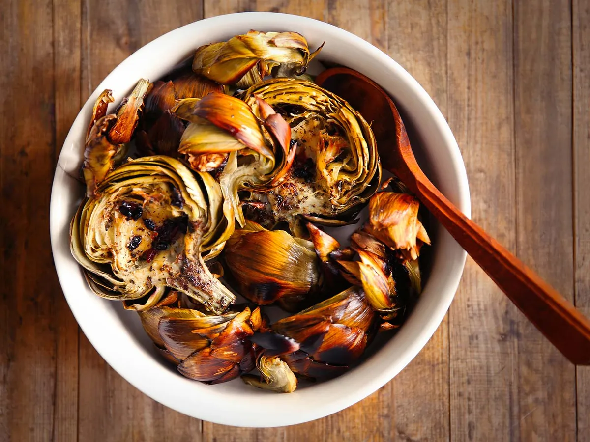 Plat de fonds d'artichaut braisés, caramélisés, dans une cocotte en terre avec herbes et quartiers de citron