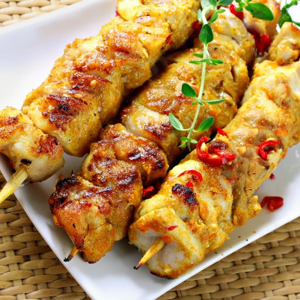 Brochettes dorées de poulet sur grille, garnies de quartiers de citron et de persil, posées sur une planche en bois