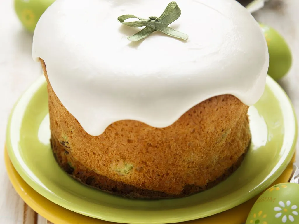Un bol de glaçage blanc et lisse posé sur un plan de travail en bois, à côté d'un fouet et de biscuits ronds en attente de décoration
