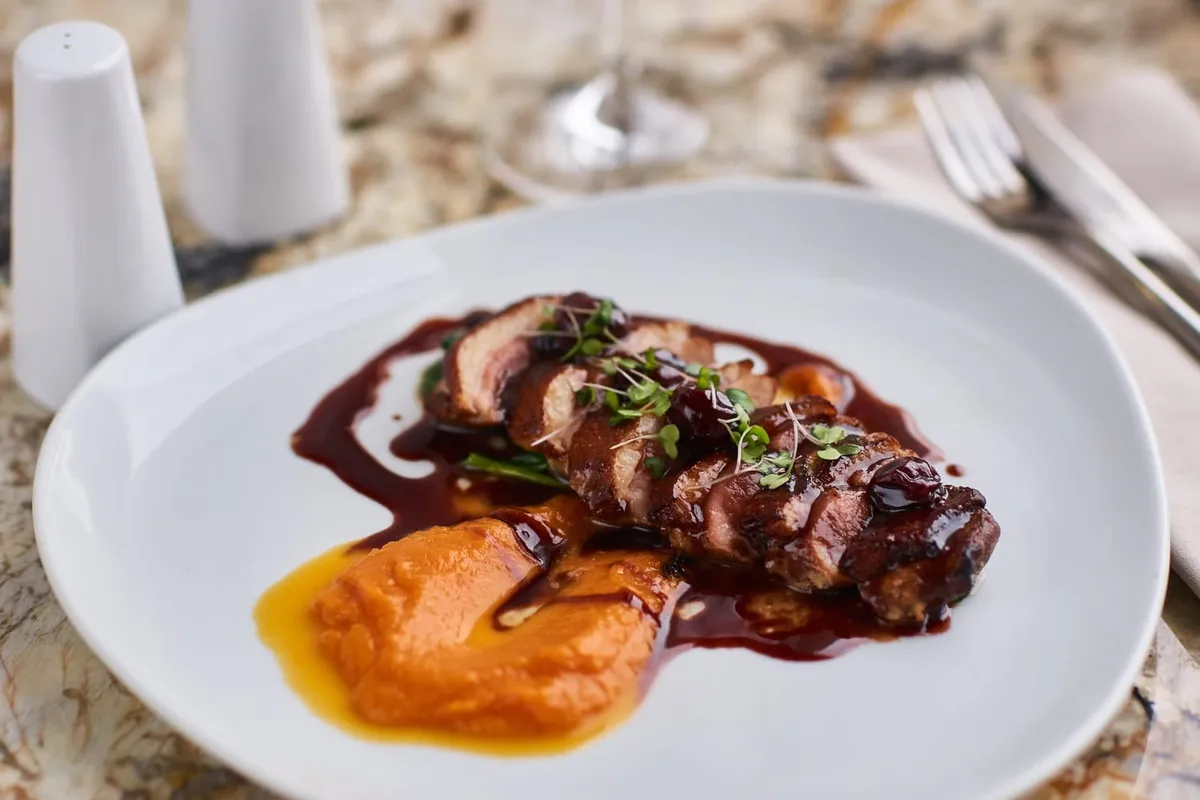 Magret de canard tranché, nappé d'une sauce brillante, quartiers d'orange et branche de thym posés sur une planche en bois