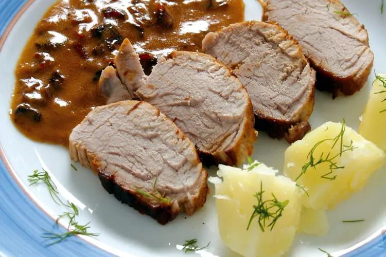 Assiette blanche avec des tranches de filet mignon nappées d'une sauce brune, purée crémeuse à côté, lumière douce et plan de travail en bois.