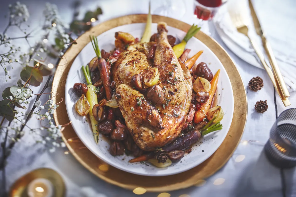 Une poularde dorée au four, entourée de légumes rôtis et d’un jus brillant dans un plat en terre