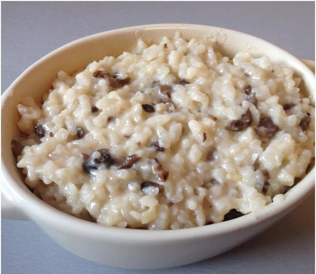 Un bol de risotto crémeux garni de lamelles de champignons sautés et d'une branche de persil, posé sur une table en bois clair