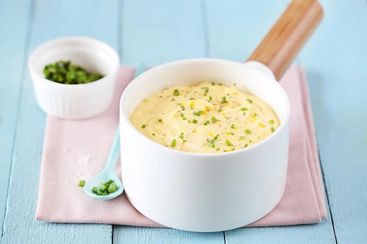 Une casserole avec une sauce dorée et onctueuse, un demi-citron pressé posé à côté sur un plan de travail en bois