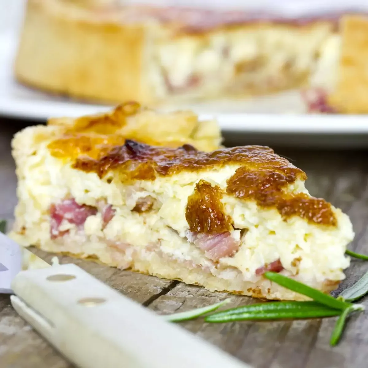 Une quiche lorraine dorée sortant du four dans un plat en terre cuite, posée sur un torchon à carreaux